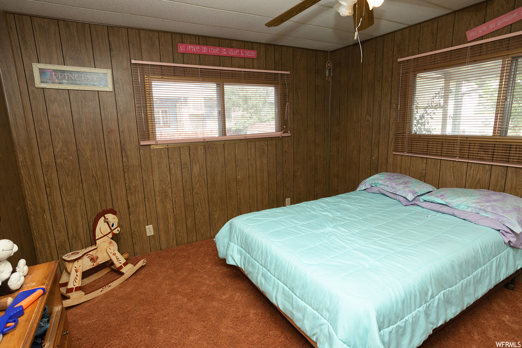 Carpeted bedroom featuring ceiling fan and wooden walls
