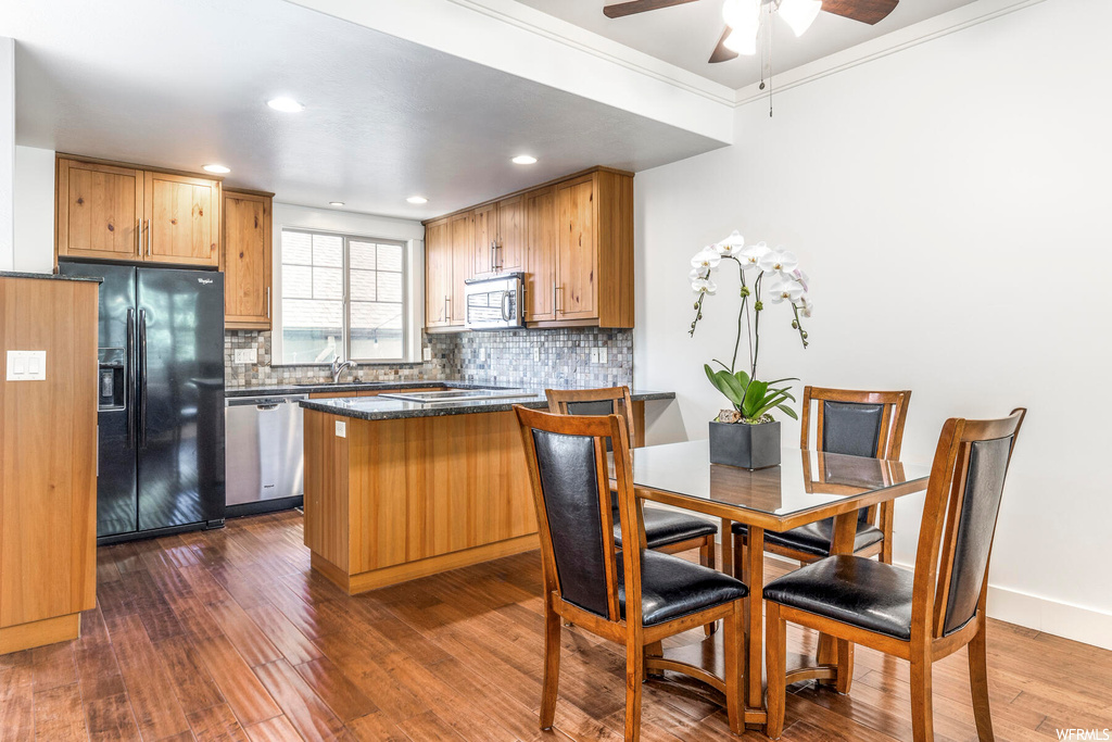 Kitchen with crown molding, light parquet floors, backsplash, brown cabinets, dark countertops, ceiling fan, and appliances with stainless steel finishes