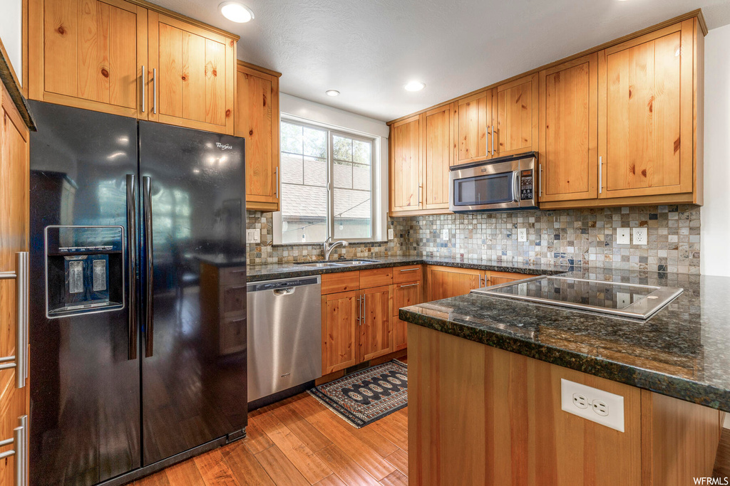 Kitchen featuring dark stone countertops, backsplash, black appliances, brown cabinets, and light hardwood flooring