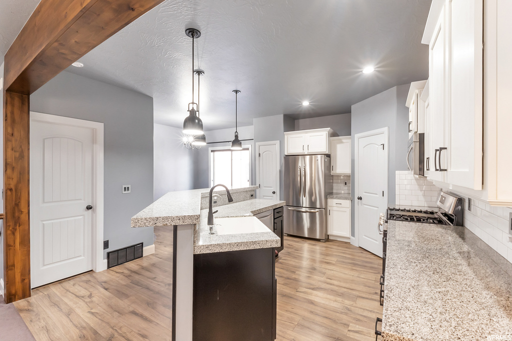 Kitchen with light hardwood flooring, light granite-like countertops, hanging light fixtures, backsplash, and stainless steel appliances