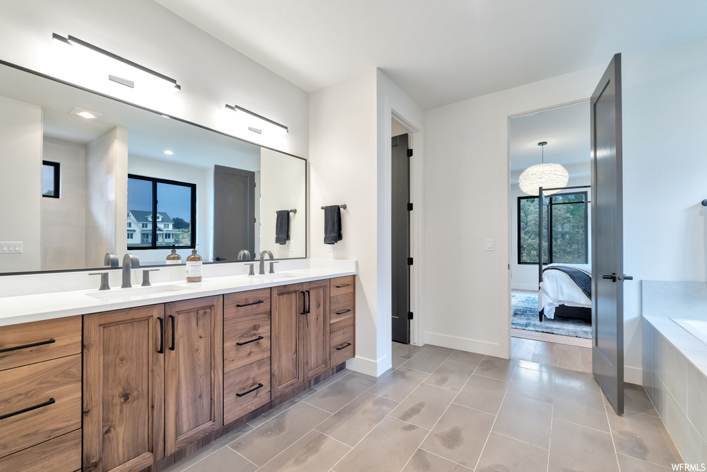 Bathroom with double sink vanity, light tile floors, a wealth of natural light, a relaxing tiled bath, and mirror
