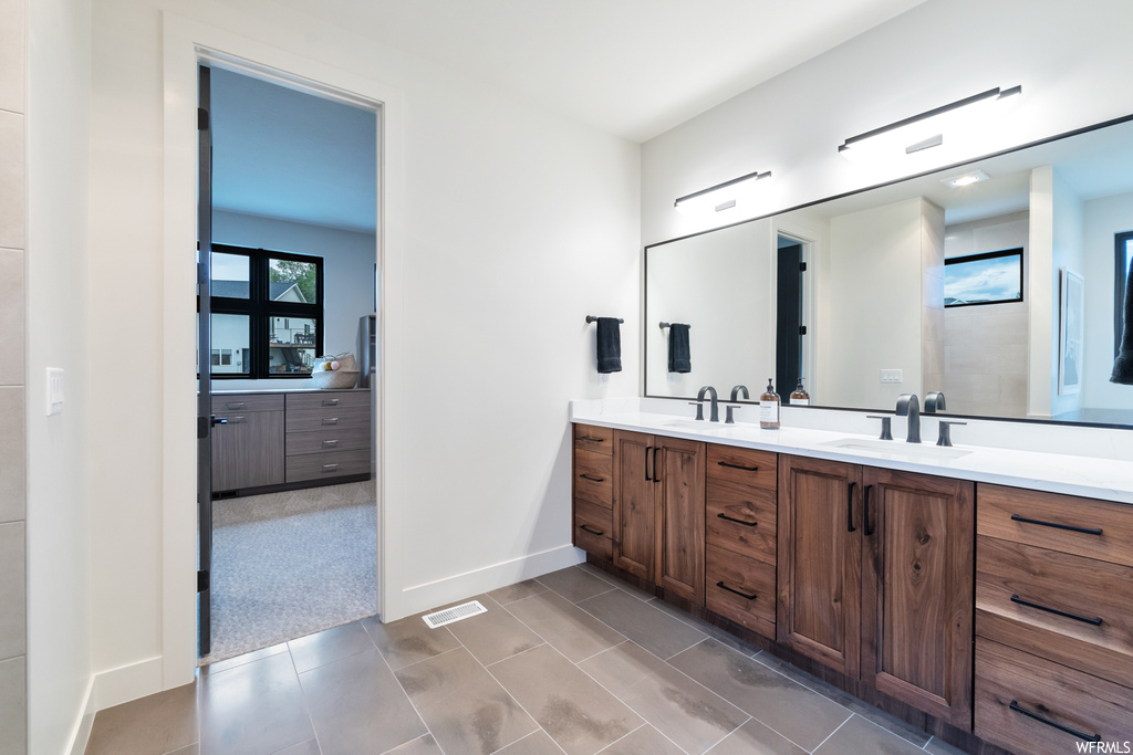 Bathroom featuring light tile floors, double sink vanity, and mirror