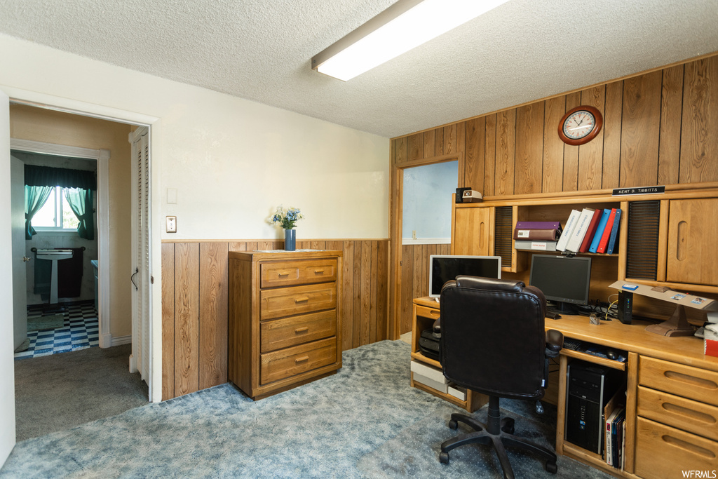 Carpeted office featuring a textured ceiling and wooden walls