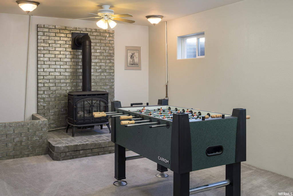 Recreation room with a fireplace, ceiling fan, and light carpet