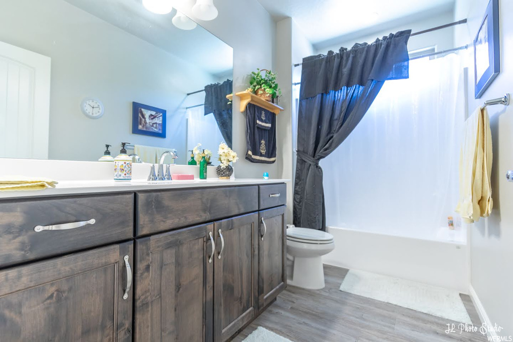 Full bathroom with large vanity, shower / bath combo with shower curtain, light hardwood flooring, and mirror