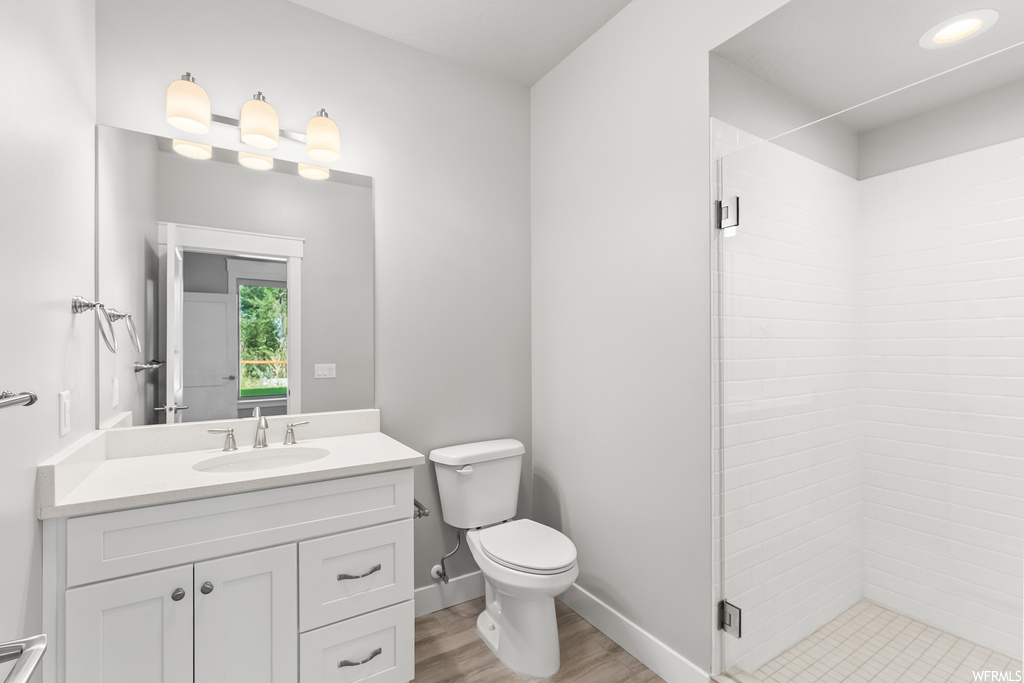 Bathroom with a tile shower, vanity, light hardwood flooring, and mirror