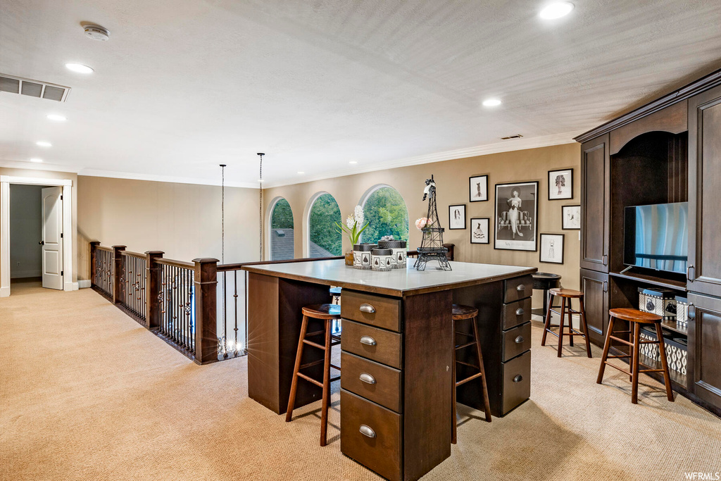 Kitchen featuring crown molding, dark brown cabinetry, light countertops, light carpet, and a center island