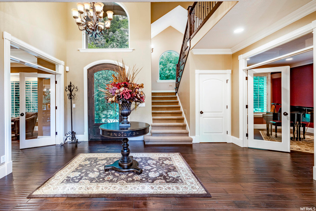 Wood floored entryway featuring crown molding, french doors, and a notable chandelier