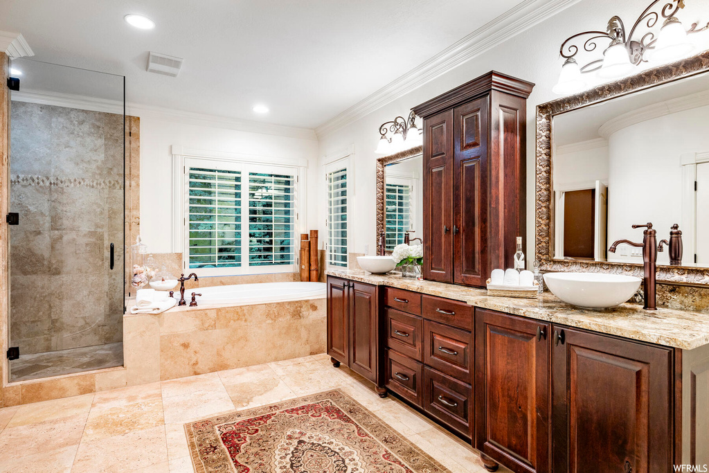 Bathroom with ornamental molding, mirror, light tile floors, separate shower and tub, and double vanity