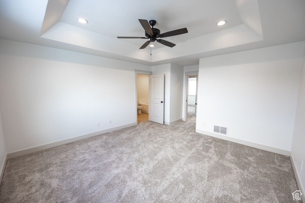 Carpeted spare room with a tray ceiling and ceiling fan