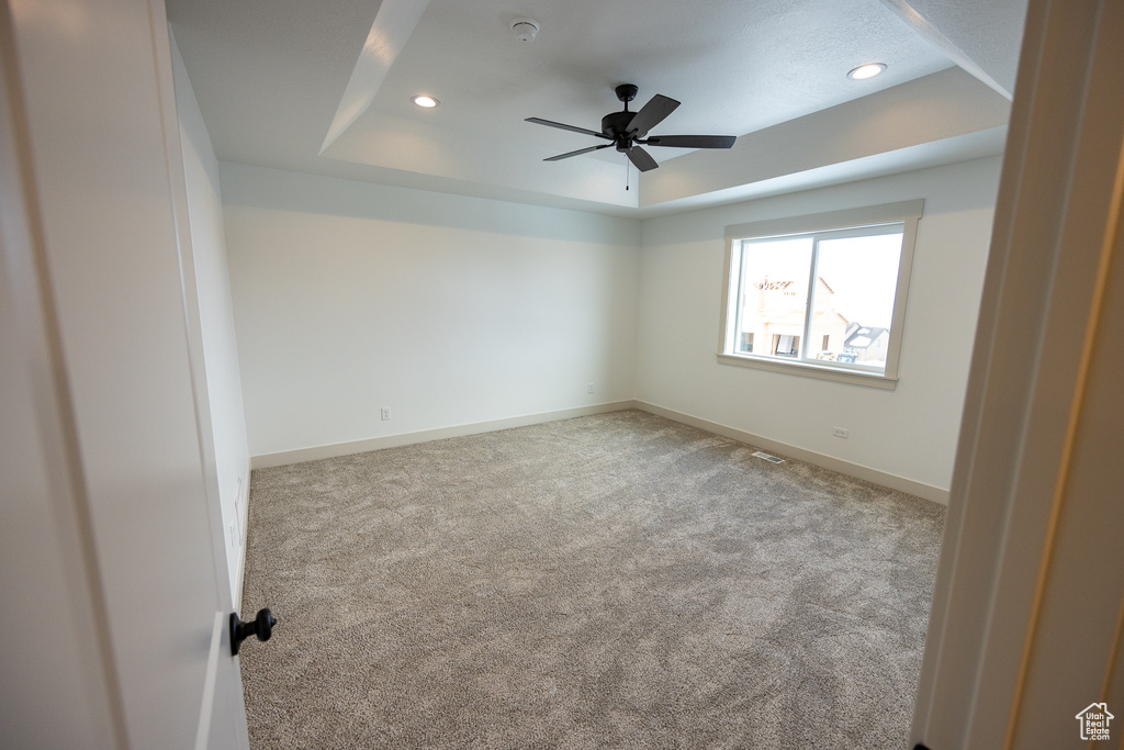 Unfurnished room with a raised ceiling, light colored carpet, and ceiling fan