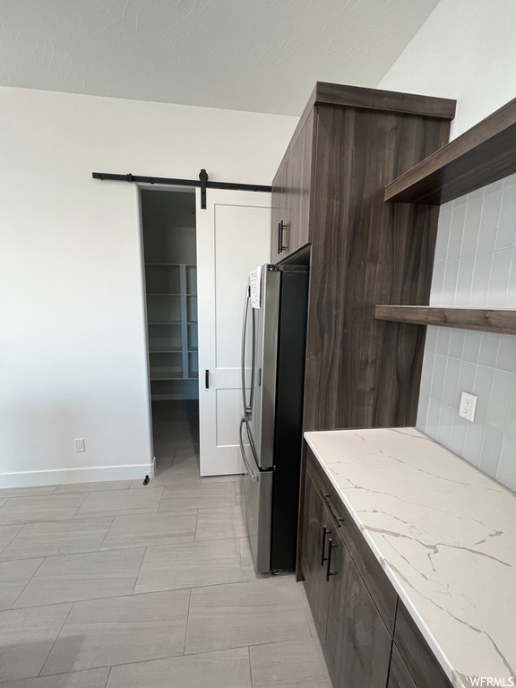 Kitchen with dark brown cabinets, stainless steel fridge, a barn door, and backsplash