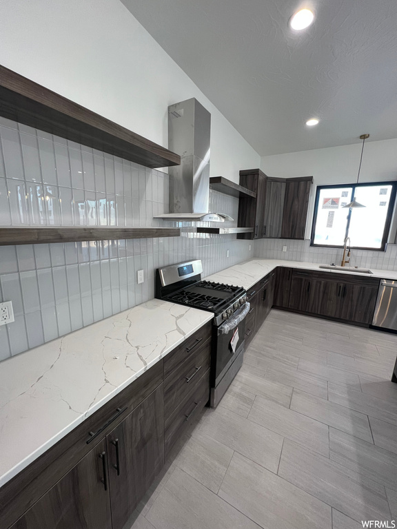 Kitchen featuring sink, light stone countertops, stainless steel appliances, wall chimney exhaust hood, and backsplash