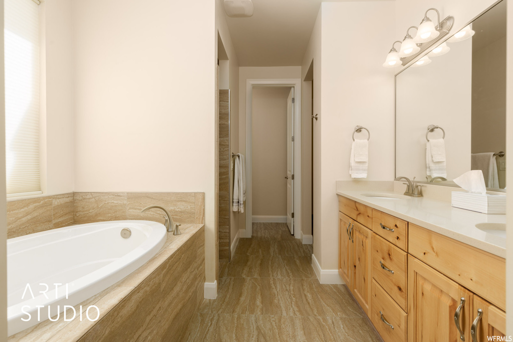 Bathroom with light tile floors, double sink vanity, a relaxing tiled bath, and mirror