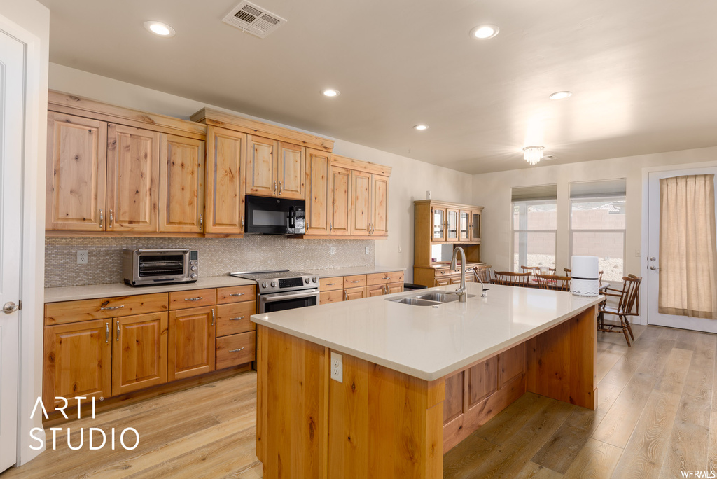 Kitchen with stainless steel range, brown cabinets, light countertops, backsplash, and light hardwood floors