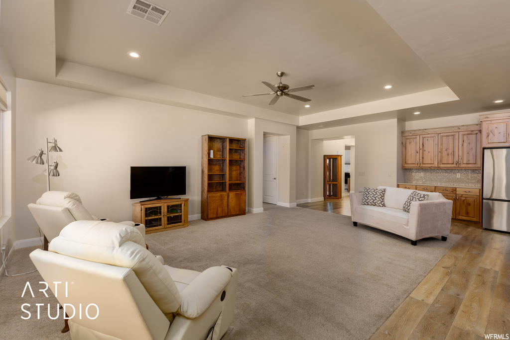 Living room with a raised ceiling, ceiling fan, and light hardwood floors
