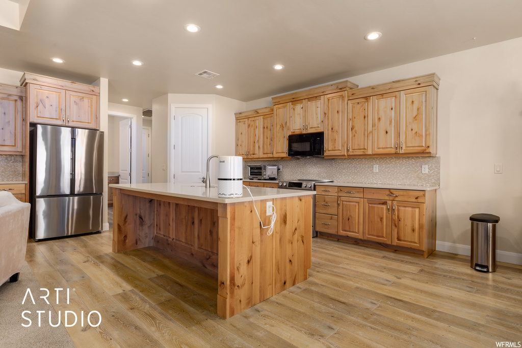 Kitchen with stainless steel fridge, brown cabinets, light countertops, backsplash, and light hardwood floors