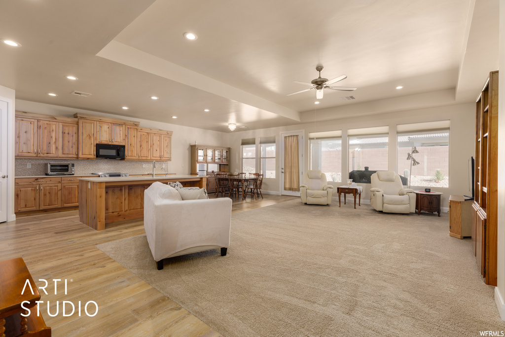 Carpeted living room featuring a raised ceiling and ceiling fan