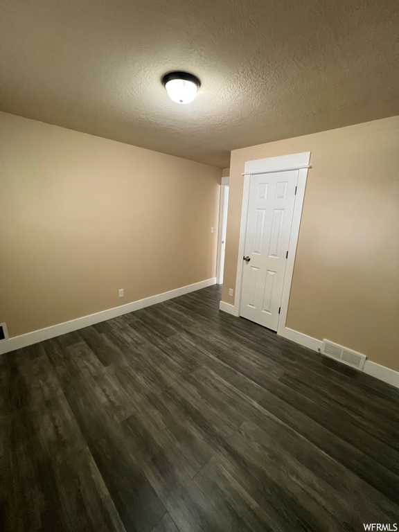 Unfurnished room with dark hardwood flooring and a textured ceiling