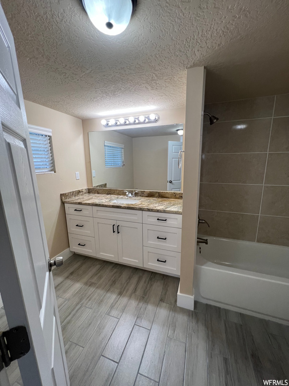 Bathroom featuring a textured ceiling, tiled shower / bath, hardwood flooring, vanity, and mirror