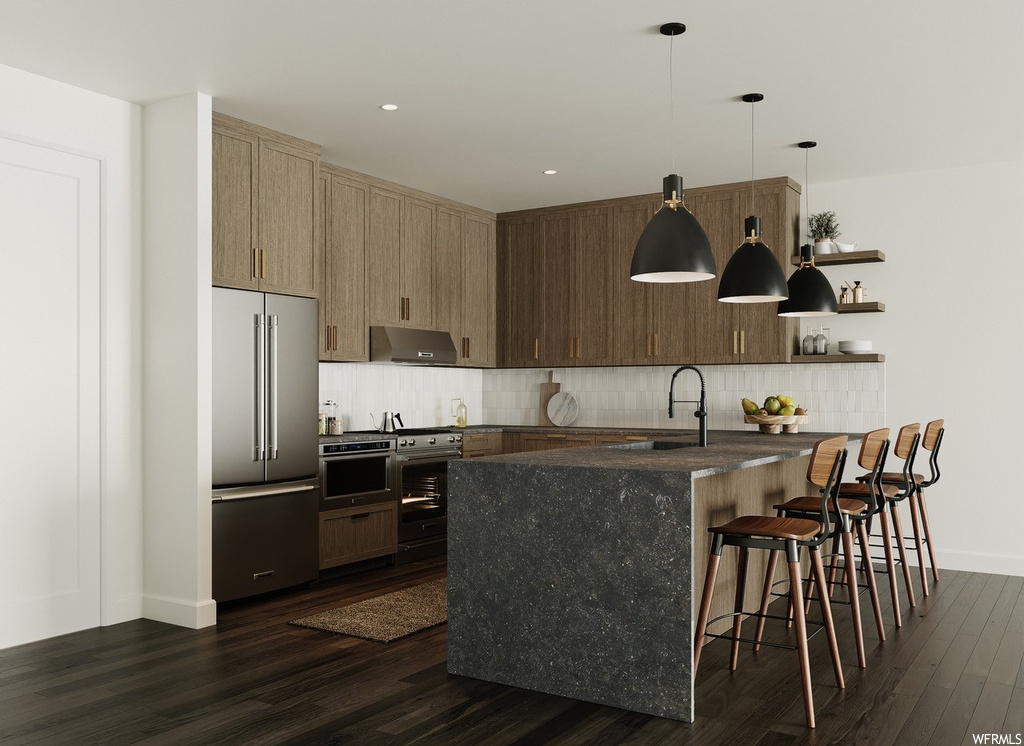 Kitchen featuring dark countertops, appliances with stainless steel finishes, dark hardwood flooring, decorative light fixtures, backsplash, and a center island