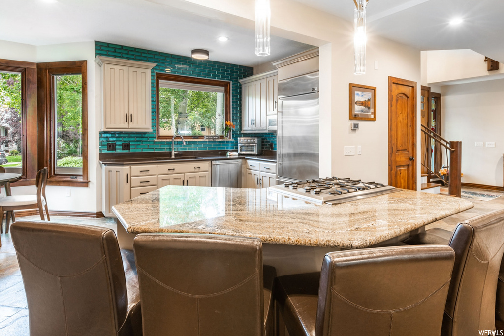 Kitchen with appliances with stainless steel finishes, a kitchen island, backsplash, light stone countertops, and tile floors