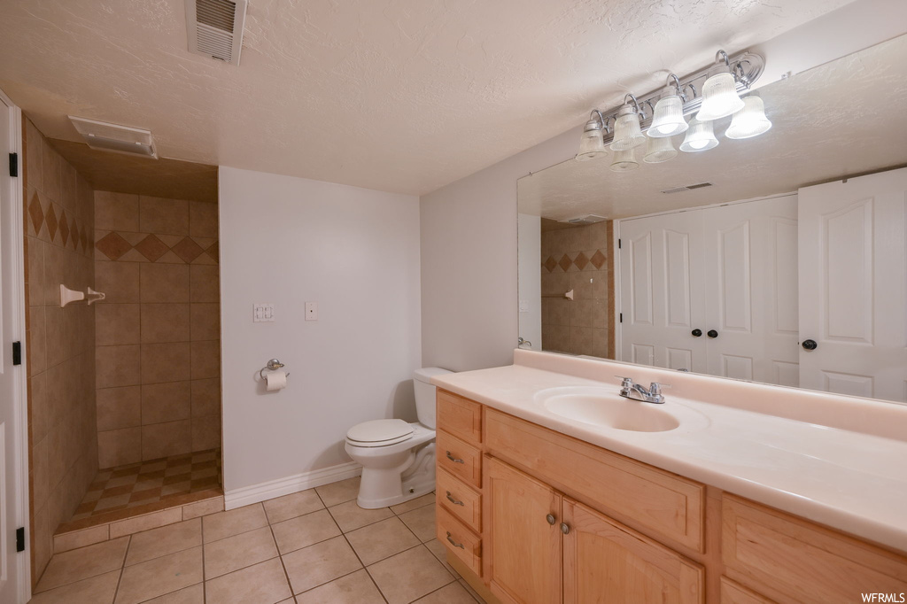 Bathroom featuring oversized vanity, tiled shower, light tile flooring, and mirror