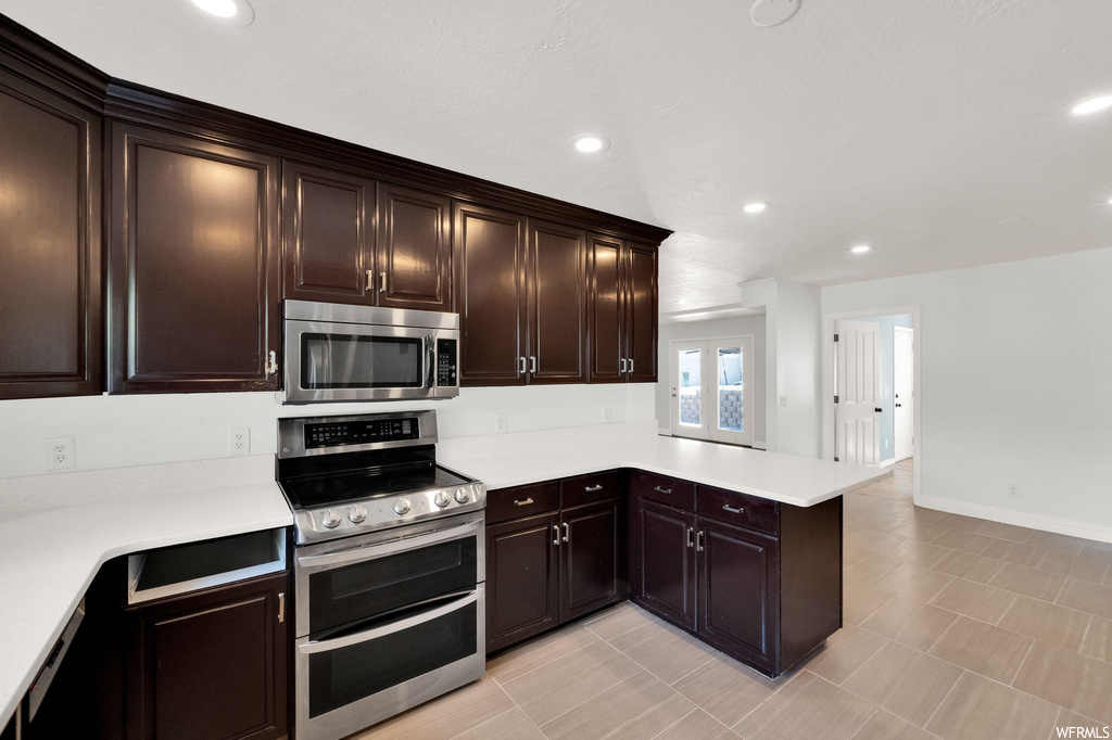 Kitchen with stainless steel appliances, light tile floors, light countertops, and dark brown cabinetry