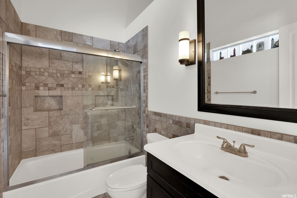 Full bathroom featuring tile walls, vanity, shower / bath combination with glass door, and mirror