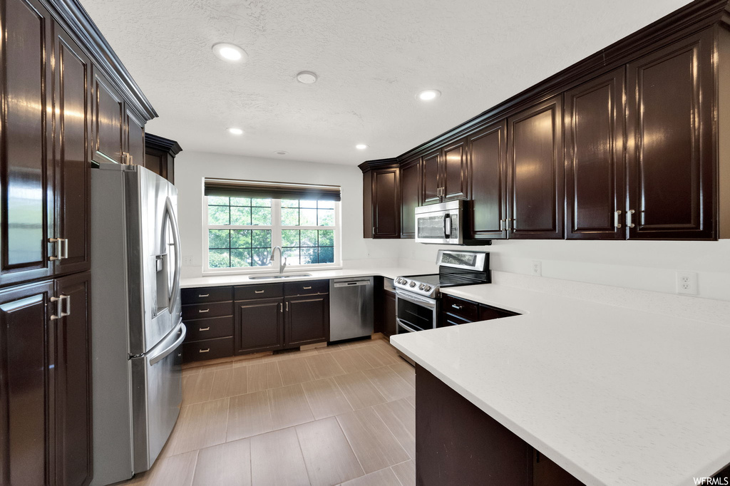 Kitchen with dark brown cabinets, stainless steel appliances, light tile flooring, and light countertops