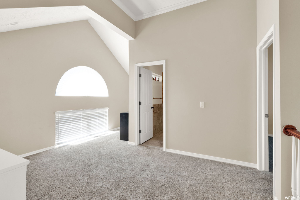Unfurnished room featuring crown molding, vaulted ceiling, a high ceiling, and light carpet