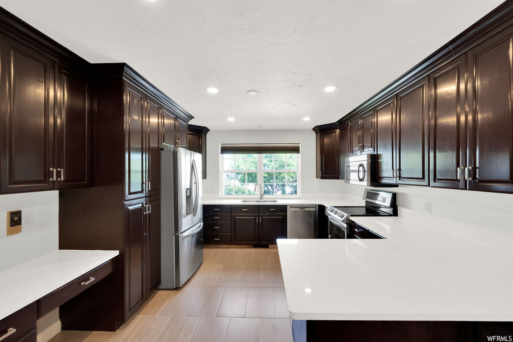 Kitchen with dark brown cabinets, appliances with stainless steel finishes, light countertops, and light tile floors