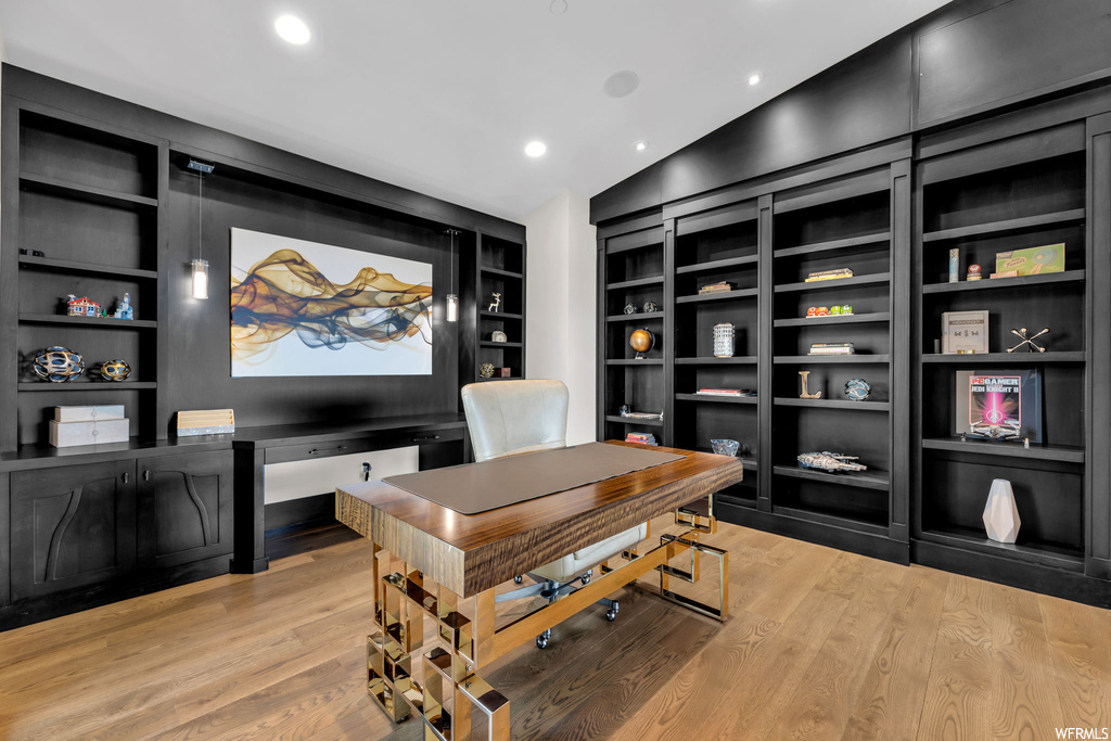 Wood floored office featuring built in shelves and lofted ceiling