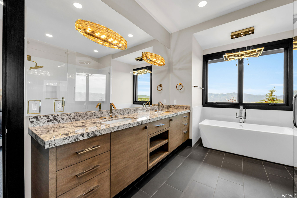 Bathroom featuring dark tile floors, dual vanity, mirror, and shower with separate bathtub