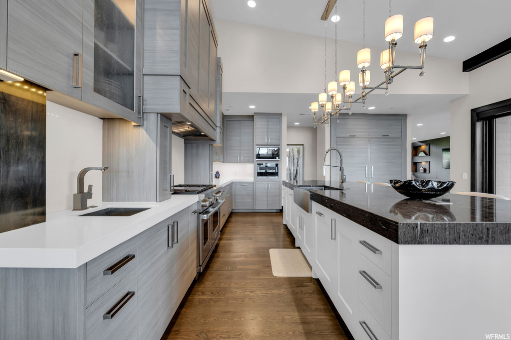 Kitchen featuring a chandelier, vaulted ceiling, dark parquet floors, hanging light fixtures, double oven range, light countertops, backsplash, and a high ceiling