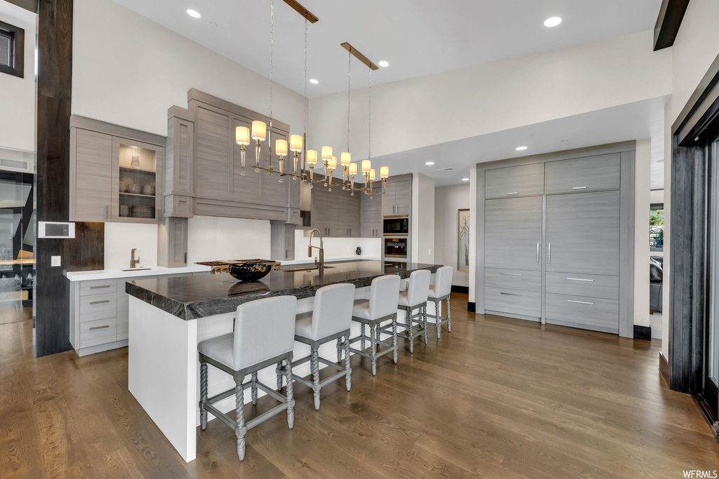 Kitchen with light hardwood floors, dark countertops, a kitchen island, hanging light fixtures, backsplash, black oven, a high ceiling, and white cabinetry