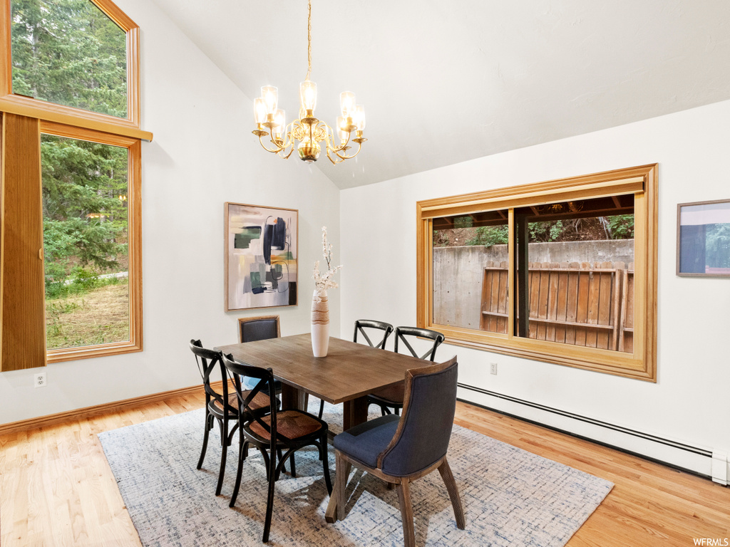 Dining room featuring light hardwood flooring, a notable chandelier, lofted ceiling, a baseboard heating unit, and a high ceiling