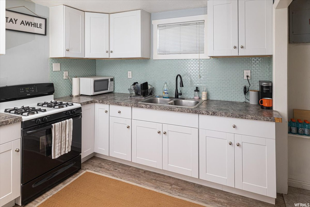 Kitchen featuring backsplash, dark countertops, white appliances, light hardwood floors, and white cabinetry