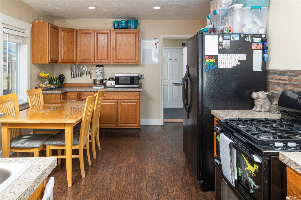 Kitchen featuring brown cabinets, dark countertops, a textured ceiling, dark hardwood flooring, and black gas range