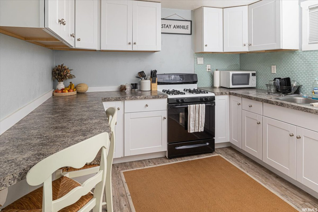 Kitchen featuring backsplash, dark countertops, hardwood floors, white appliances, and white cabinets