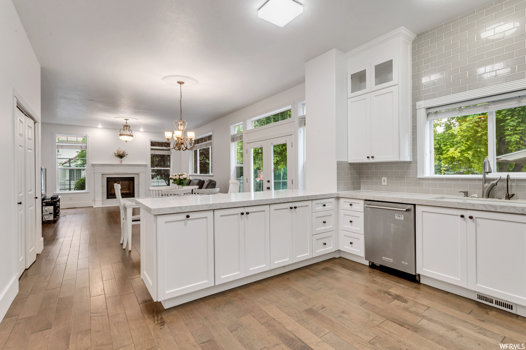 Kitchen featuring white cabinets, light parquet floors, a fireplace, light countertops, stainless steel dishwasher, and backsplash