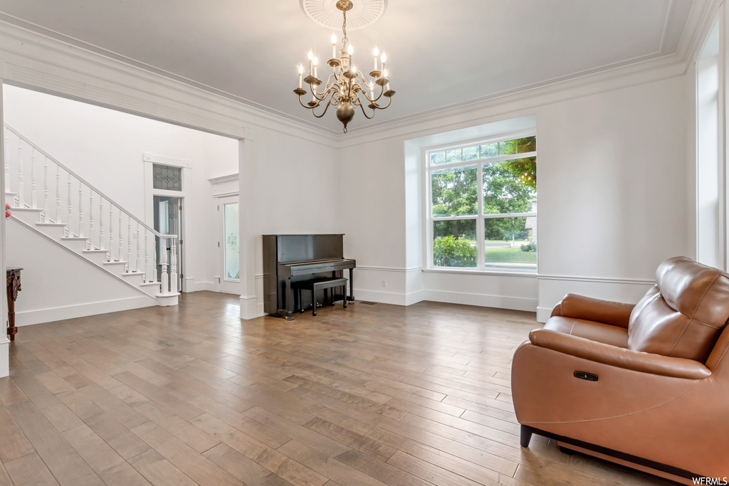 Interior space featuring ornamental molding, light hardwood flooring, and a notable chandelier