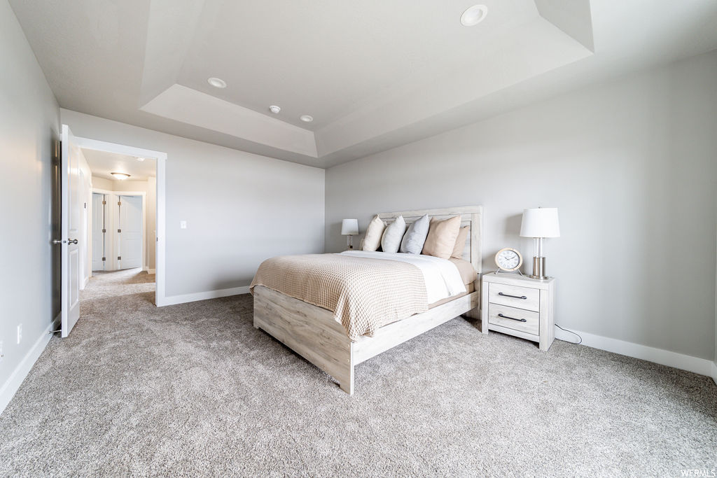 Bedroom with a raised ceiling and light carpet