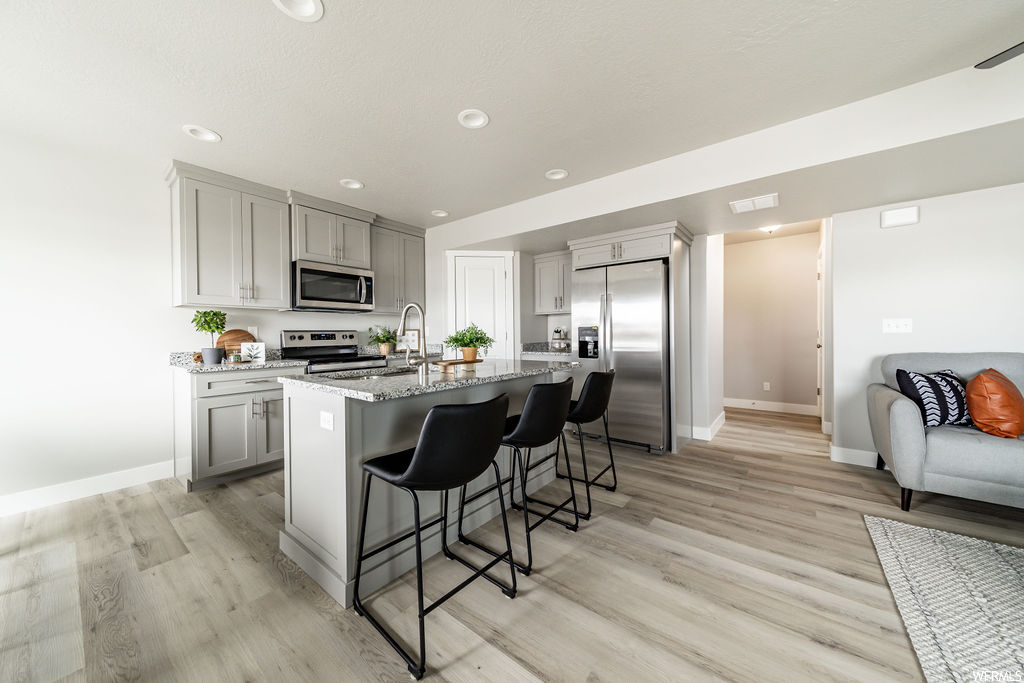 Kitchen featuring stainless steel appliances, light countertops, light hardwood floors, white cabinetry, and a center island