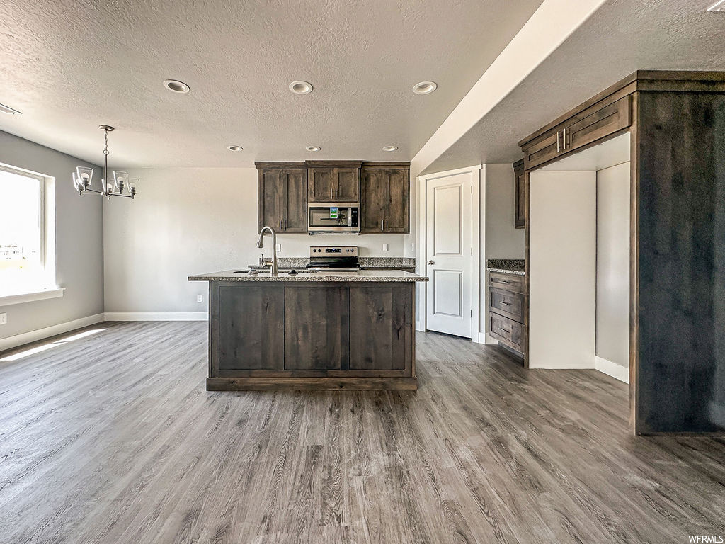 Kitchen featuring a textured ceiling, light parquet floors, an island with sink, dark brown cabinetry, and appliances with stainless steel finishes