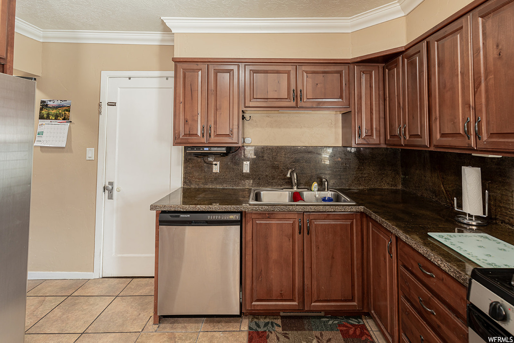 Kitchen featuring tasteful backsplash, light tile floors, stainless steel appliances, sink, and dark stone countertops