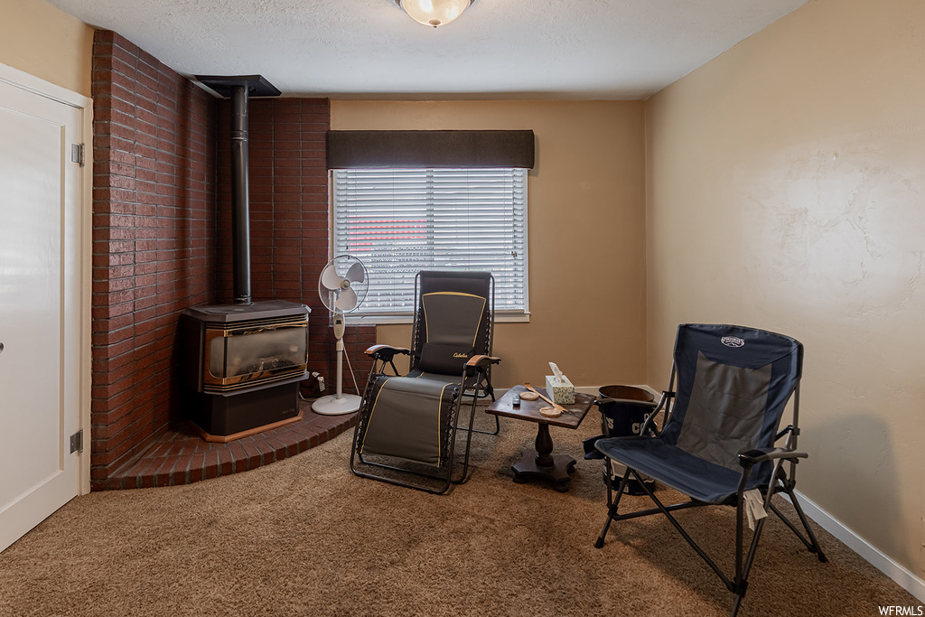 Sitting room featuring carpet floors, a wood stove, brick wall, and a textured ceiling