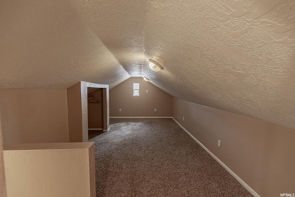 Additional living space featuring a textured ceiling, vaulted ceiling, and dark colored carpet