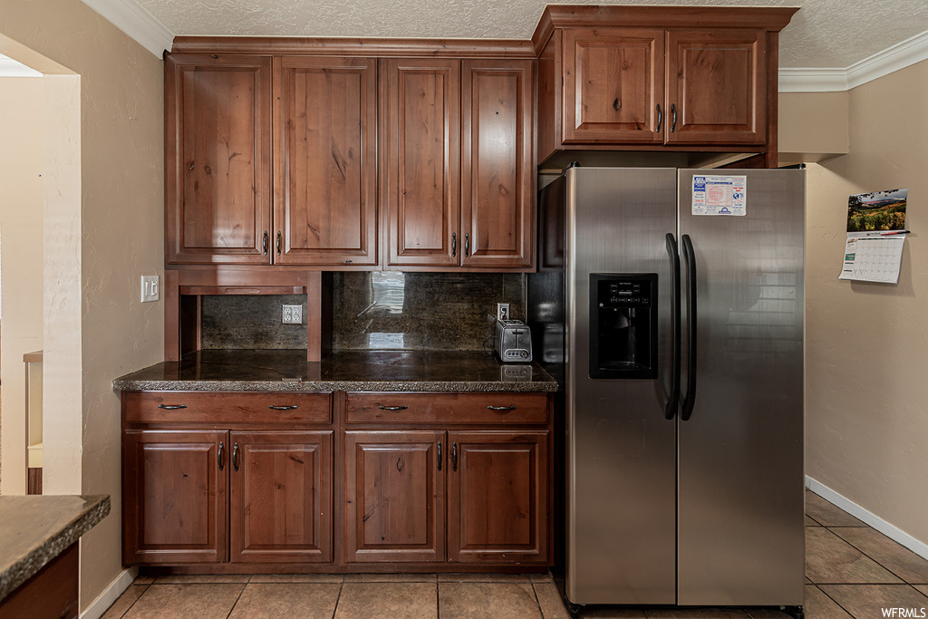 Kitchen with stainless steel fridge with ice dispenser, dark stone countertops, and ornamental molding