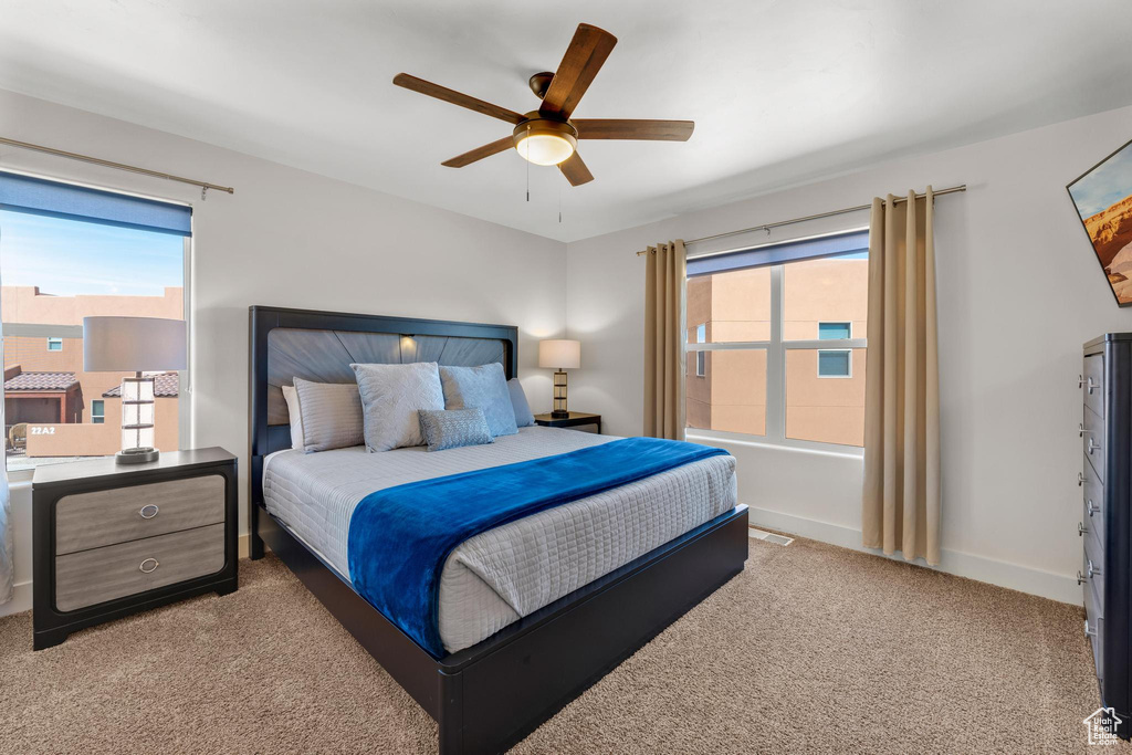 Bedroom featuring multiple windows, light colored carpet, and ceiling fan